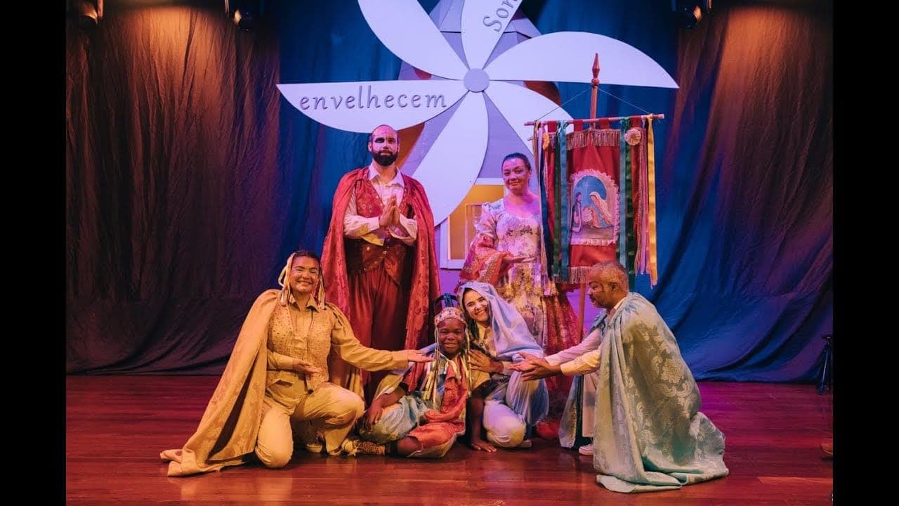 The cast onstage in folk-festival costumes, in front of a giant pinwheel.