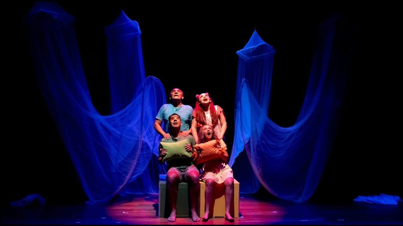 Quatro atores de pijama sobre uma cama no palco, sob luz azul e tecidos.