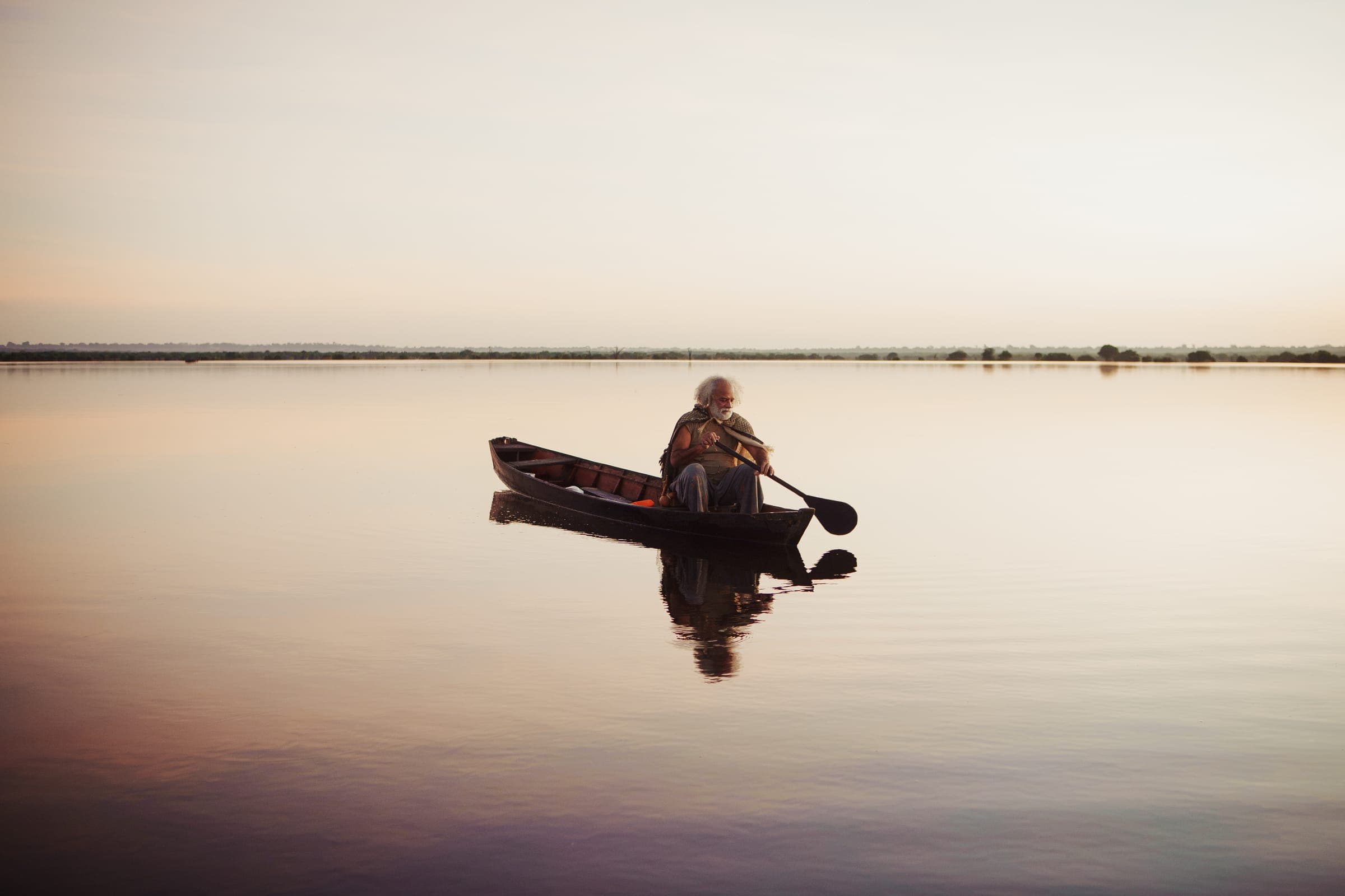 Hombre en una canoa, remando en el lago quieto al atardecer.